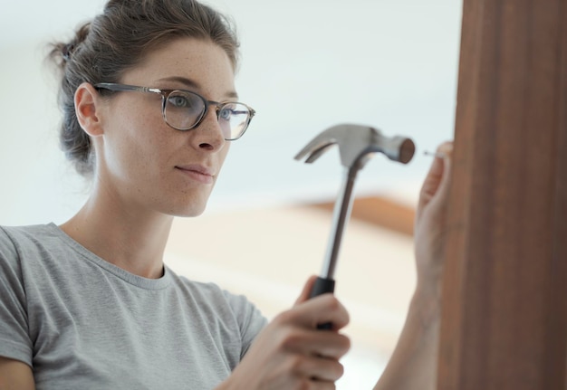 Mujer reparando una puerta en casa usando un martillo para la renovación del hogar y el concepto de bricolaje