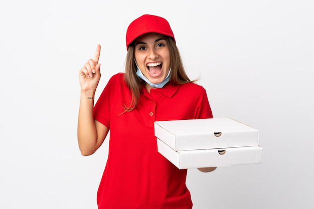 Mujer repartidora de pizzas sosteniendo una pizza y protegiéndose del coronavirus con una máscara sobre una pared blanca aislada apuntando una gran idea