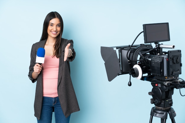 Mujer reportera sosteniendo un micrófono y reportando noticias aisladas en azul