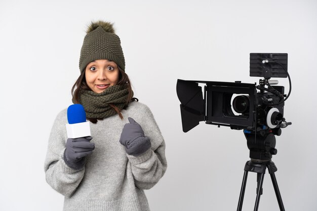 Mujer reportera sosteniendo un micrófono y reportando noticias sobre fondo blanco aislado con expresión facial sorpresa