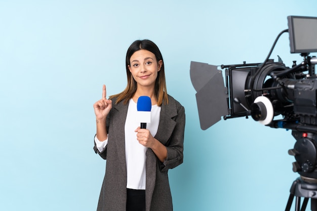 Foto mujer reportera sosteniendo un micrófono y reportando noticias sobre la pared azul señalando con el dedo índice una gran idea