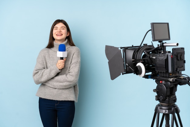 Mujer reportera sosteniendo un micrófono y reportando noticias sobre pared azul