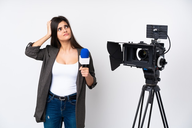 Foto mujer reportera sosteniendo un micrófono y reportando noticias sobre una pared blanca con dudas y con expresión de la cara confundida