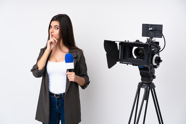 Mujer reportera sosteniendo un micrófono y reportando noticias sobre pared blanca haciendo gesto de silencio