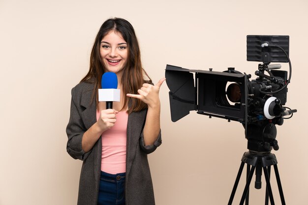 Mujer reportera sosteniendo un micrófono y reportando noticias sobre pared haciendo gesto de teléfono