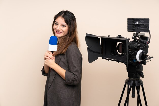 Mujer reportera sosteniendo un micrófono y reportando noticias sobre la pared riendo