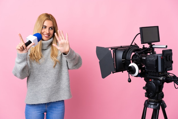 Mujer reportera sosteniendo un micrófono y reportando noticias sobre la pared rosa contando siete con los dedos