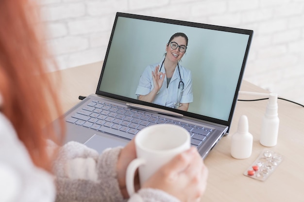 Una mujer con un resfriado está de baja por enfermedad y está mirando una videoconsulta portátil con un médico amable Un paciente en una cita remota Reunión en línea