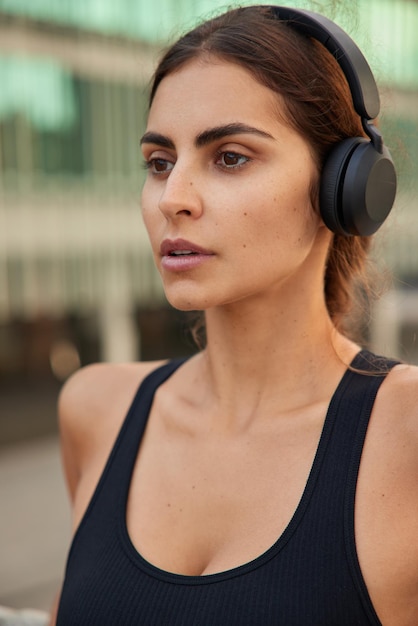 mujer respira profundamente con expresión motivada practica deporte tiene entrenamiento matutino usa auriculares estéreo inalámbricos en los oídos para escuchar música