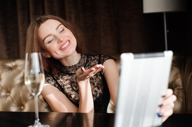 Mujer en un restaurante relajante con copa de champán y tablet pc.