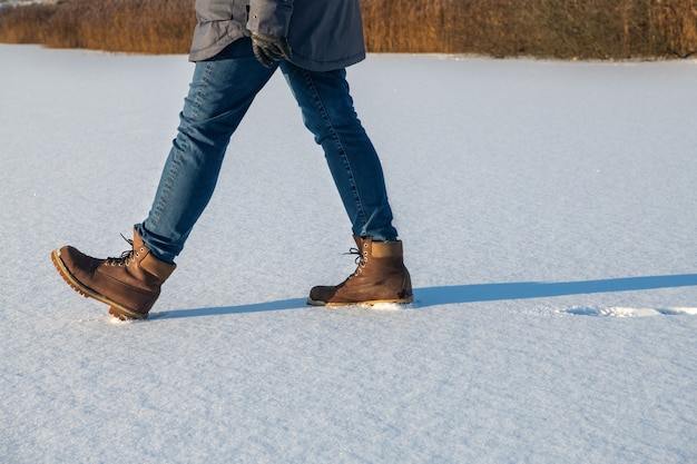 La mujer se retrasa en botas caminando sobre nieve fresca en invierno. Primer plano de zapatos de invierno.