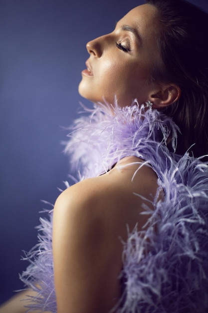 Una mujer retratada con un vestido morado de noche con plumas se encuentra en el fondo del estudio