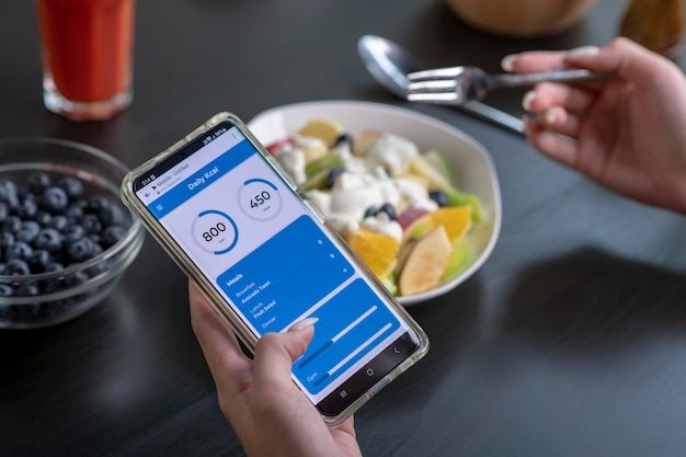 Mujer revisando la aplicación de calorías y nutrientes en su teléfono mientras come Nutricionista profesional