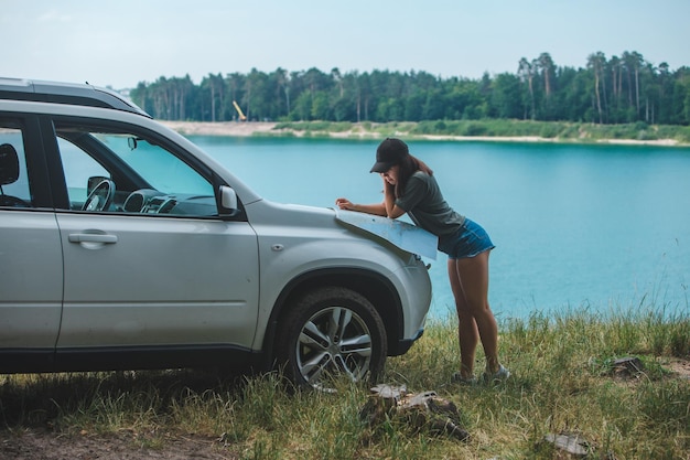 Mujer revisando con el mapa en el lago del capó del automóvil suv con agua azul en el fondo