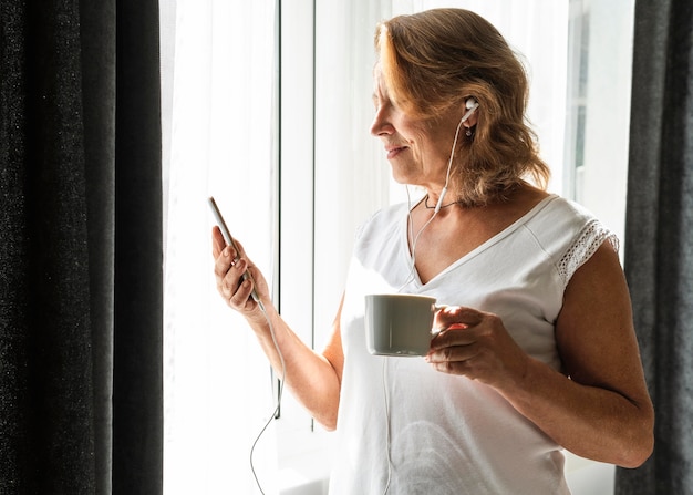 Mujer revisando su teléfono en casa mientras el distanciamiento social