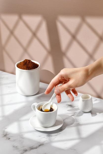 Mujer revuelva el café con una cuchara de café Taza de café Fondo beige y mármol con sombra de ventana