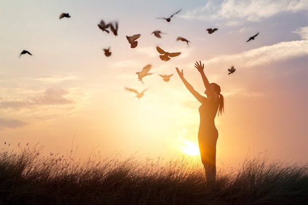 Mujer rezando y liberando a las aves a la naturaleza en el fondo del atardecer