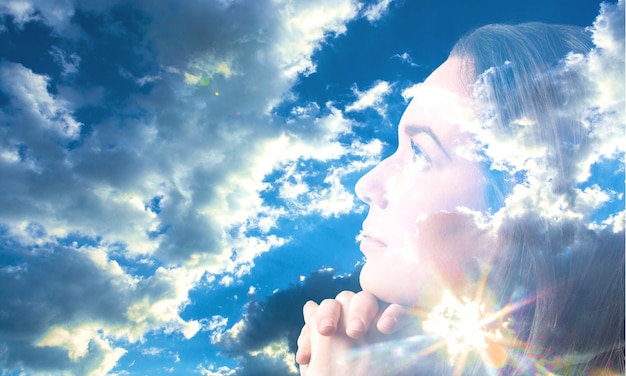 Mujer rezando sobre cielo azul con rayos de luz