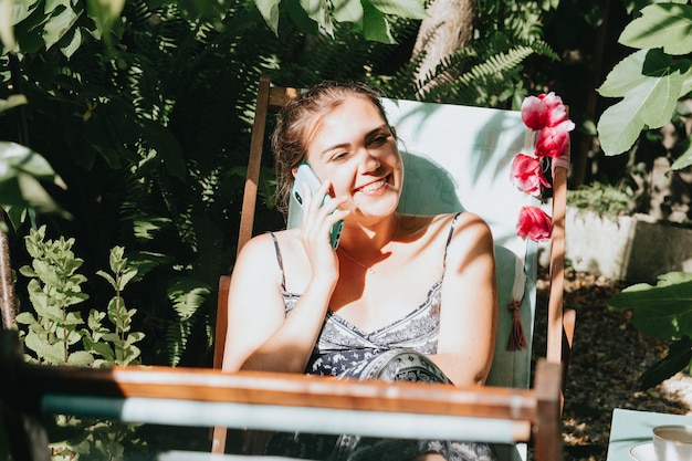 Mujer riendo mientras realiza una llamada telefónica en un jardín soleado durante las vacaciones, relajarse trabajando desde casa