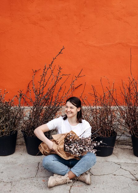 Foto mujer riendo sentada en el suelo sosteniendo un gran ramo de ramas con flores de cerezo rosadas en flor