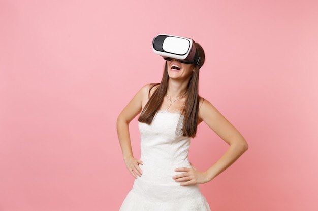 Mujer riendo con vestido blanco y auriculares de realidad virtual de pie con los brazos en jarras