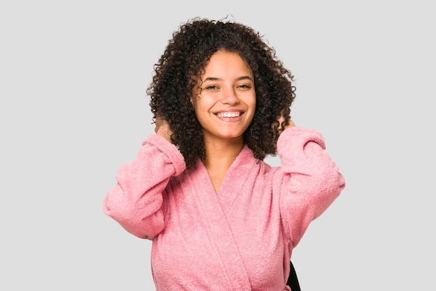 Mujer rizada afroamericana joven que lleva una bata de baño rosa aislada