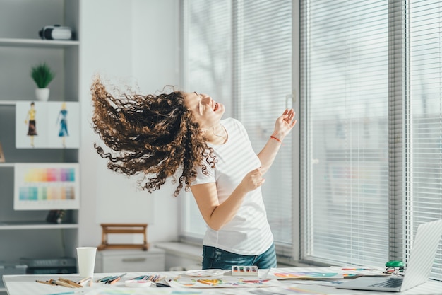 La mujer rizada bailando cerca de la mesa con un equipo de arte.