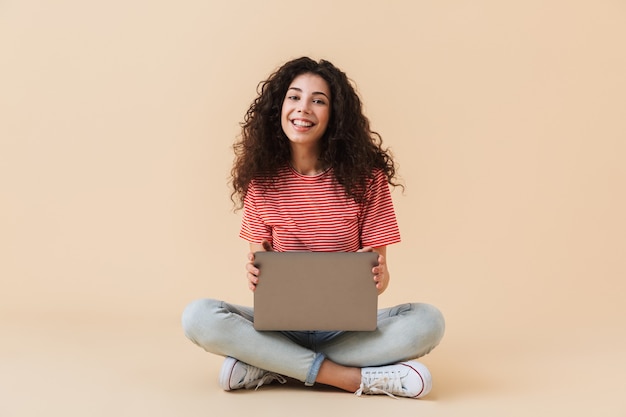 Mujer rizada bastante joven feliz usando la computadora portátil.