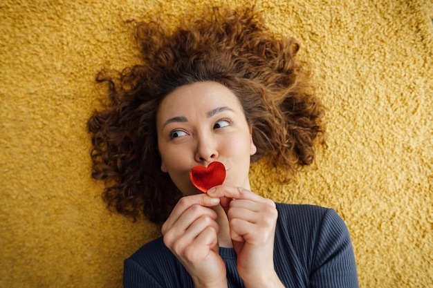 La mujer rizada coqueta envía un beso aéreo con corazones de San Valentín