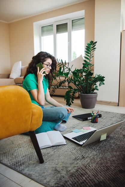 Mujer rizada en el piso usando la computadora portátil mientras hace la tarea trabajo autónomo de carrera independiente