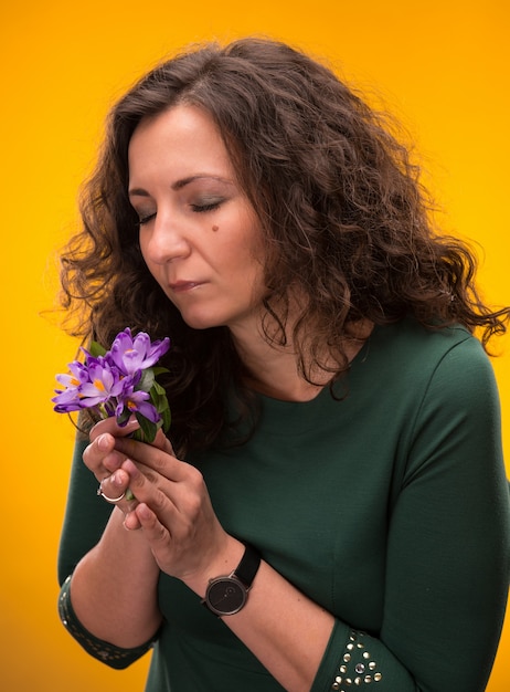 Mujer rizada que huele las flores del azafrán con los ojos cerrados sobre un fondo amarillo