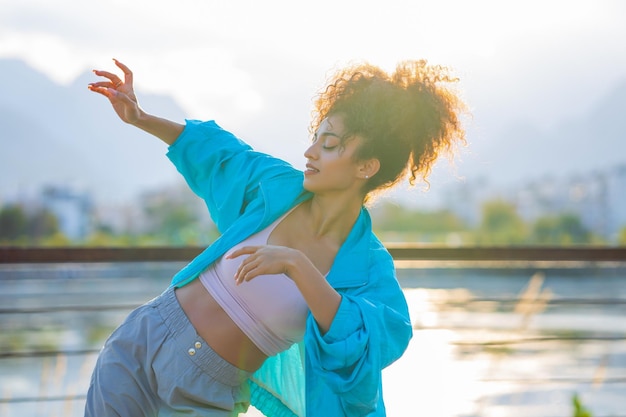 Mujer rizada de raza mixta disfrutando de la danza al atardecer en la playa