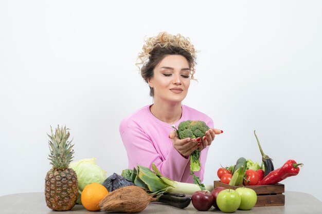 Mujer rizada sentada a la mesa con brócoli fresco.