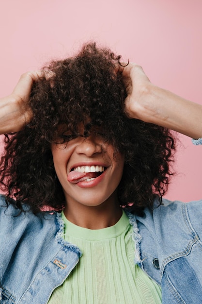 Mujer rizada sonriente en chaqueta de mezclilla posando sobre fondo rosa Chica feliz alegre en camiseta verde riendo sobre fondo aislado