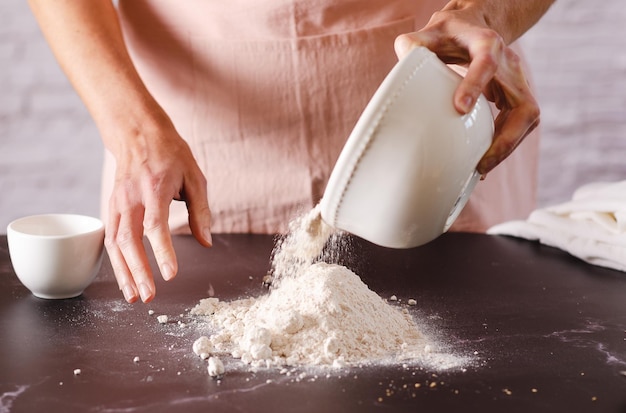 Mujer rociando harina sobre una mesa en la cocina Proceso de cocción