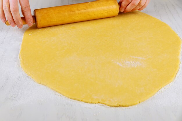 Mujer rodando masa con pin para hacer galletas en la mesa blanca