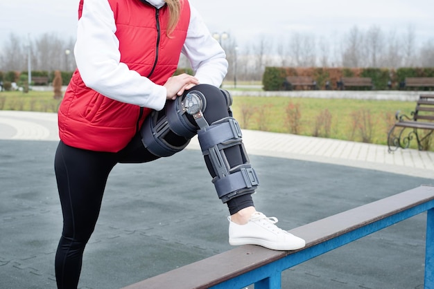 Mujer con rodillera u ortesis después de una cirugía de piernas haciendo ejercicio en el parque