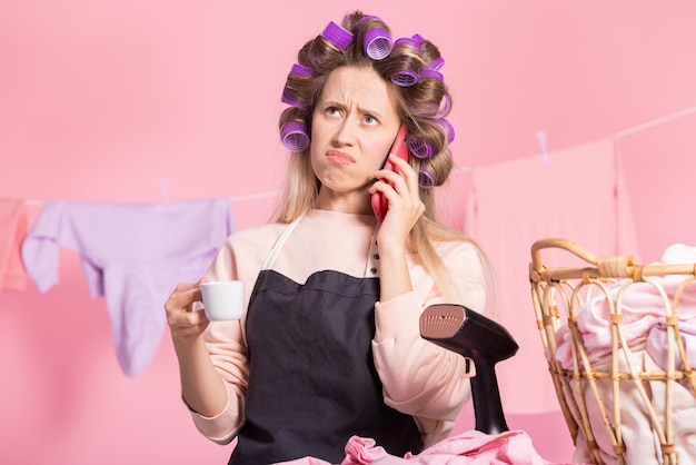 Mujer con rodillos en la cabeza para rizar el cabello bebe café de una taza habla por teléfono con su esposo