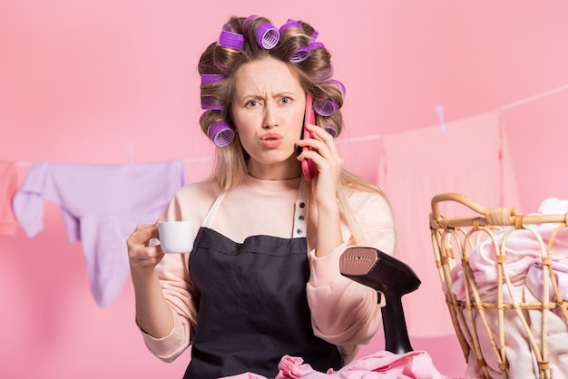 Mujer con rodillos en la cabeza para rizar el cabello bebe café de una taza habla por teléfono con su esposo