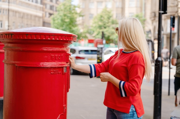 Mujer en rojo corta cartas de envío en buzón rojo en Inglaterra