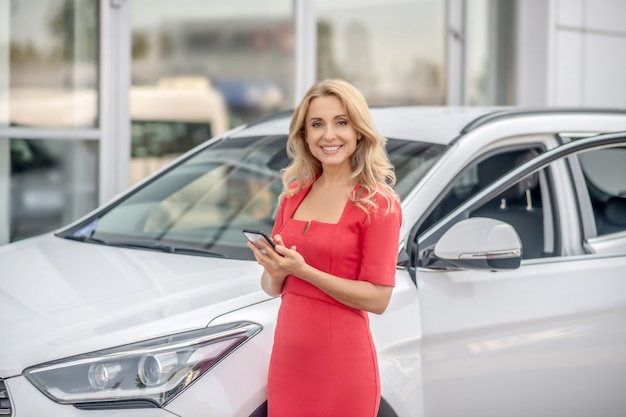 Mujer de rojo. Mujer bonita en un vestido rojo de pie cerca del coche con un teléfono en las manos