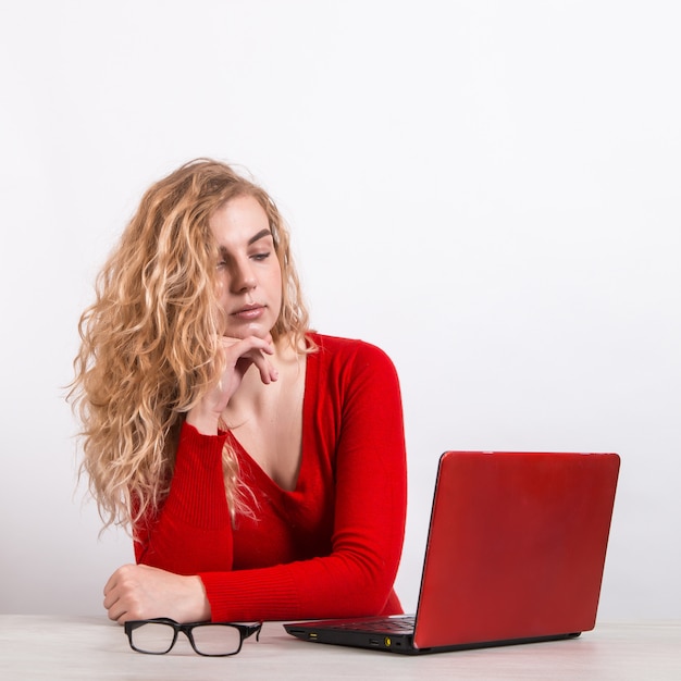 mujer en rojo, trabajando remotamente en la computadora en blanco.