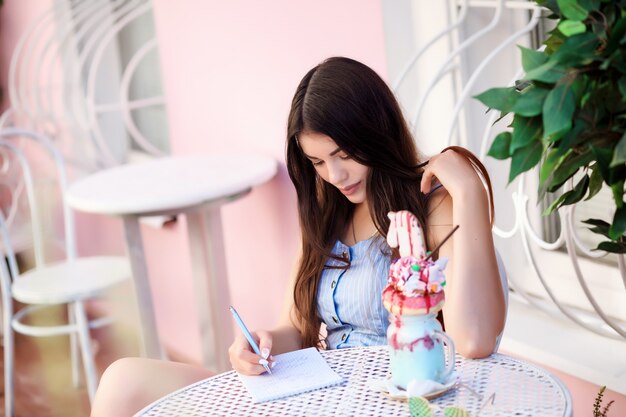 La mujer romántica está escribiendo algo en su cuaderno mientras está sentado en el café al aire libre.