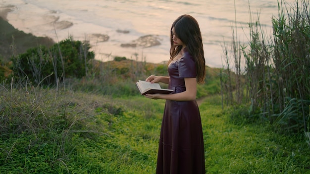 Mujer romántica mirando un libro pasando páginas en un hermoso día nublado en el océano