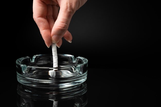 Una mujer rompe un cigarrillo sobre un fondo negro. Vista lateral con la horizontal.