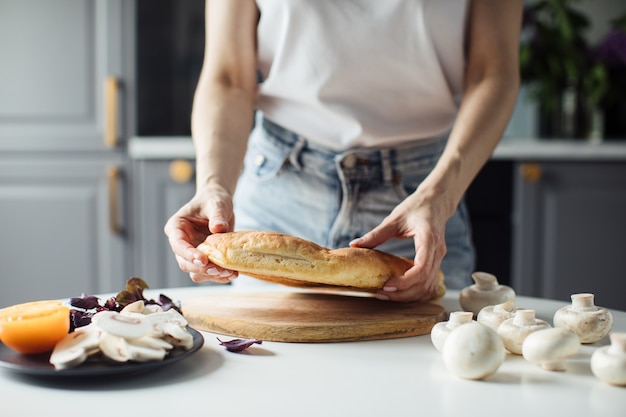 Mujer rompe el pan con las manos en la cocina luminosa