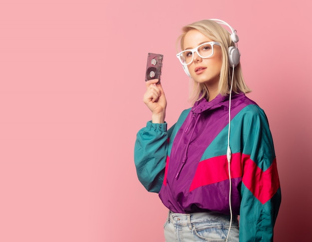 Mujer en ropa de los 90 con auriculares y cassette de audio