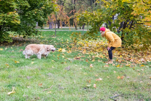 Una mujer en ropa de abrigo está llamando a su perro perdiguero entre las hojas amarillas del otoño