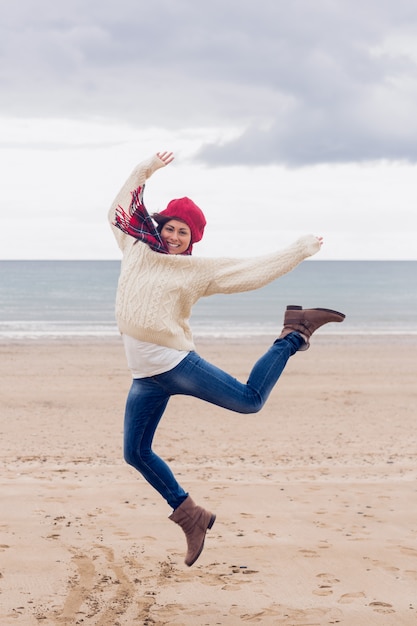 Mujer en ropa de abrigo con estilo saltando en la playa