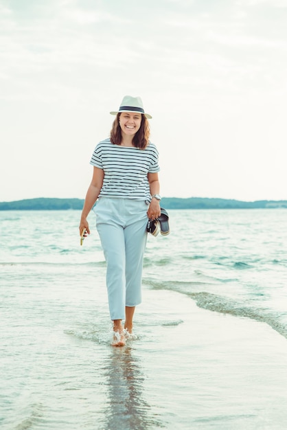 Mujer en ropa blanca caminando por la playa de mar horario de verano